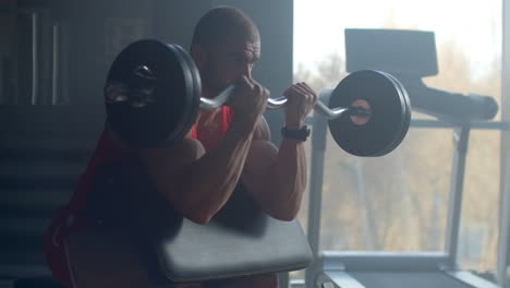 A-strong-male-bodybuilder-lifts-a-weight-barbell-while-sitting-on-a-bench-and-trains-hard-in-slow-motion-at-the-GYM.-A-bodybuilder-trains-professionally.-Powerful-strong-hands